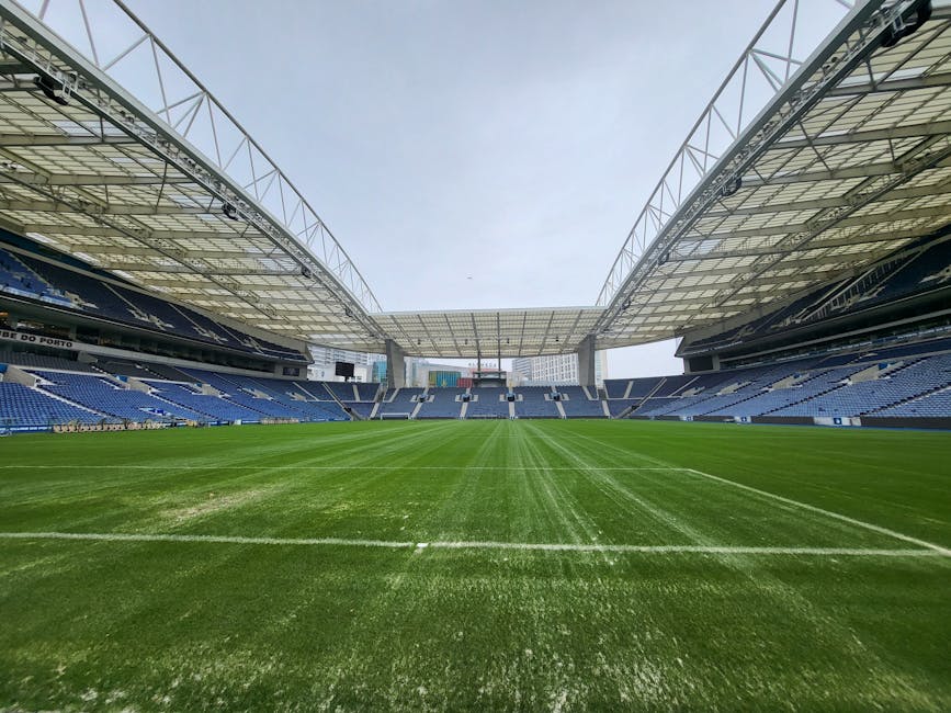 Interior view of the Tottenham Hotspur Stadium showcasing organized blue and red seating areas, including a large banner displaying the club's name, with a well-maintained grass pitch in the foregroun